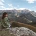 A woman in a green sweater sits on a rock, enjoying the stunning view of majestic mountains during the day.